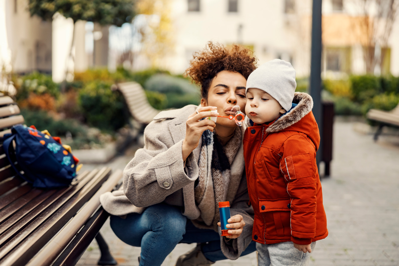 Mom and child blow bubbles outdoors on a cold day