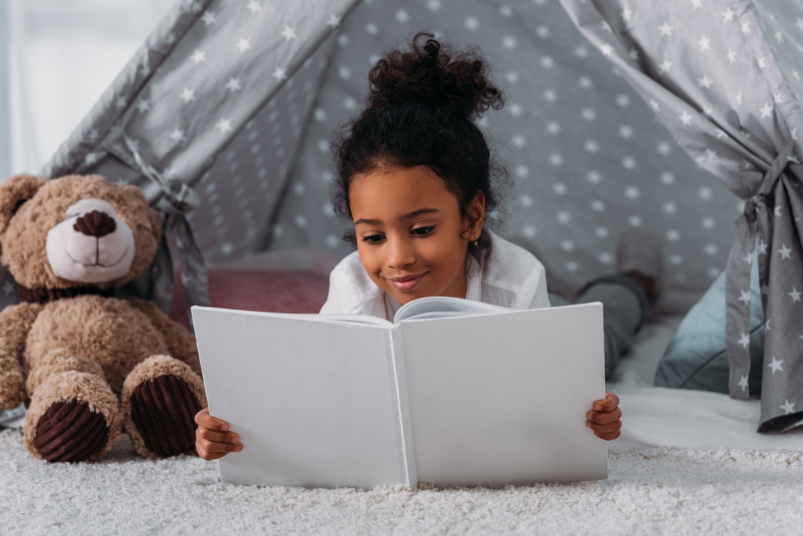 Girl sits under play tent reading a book